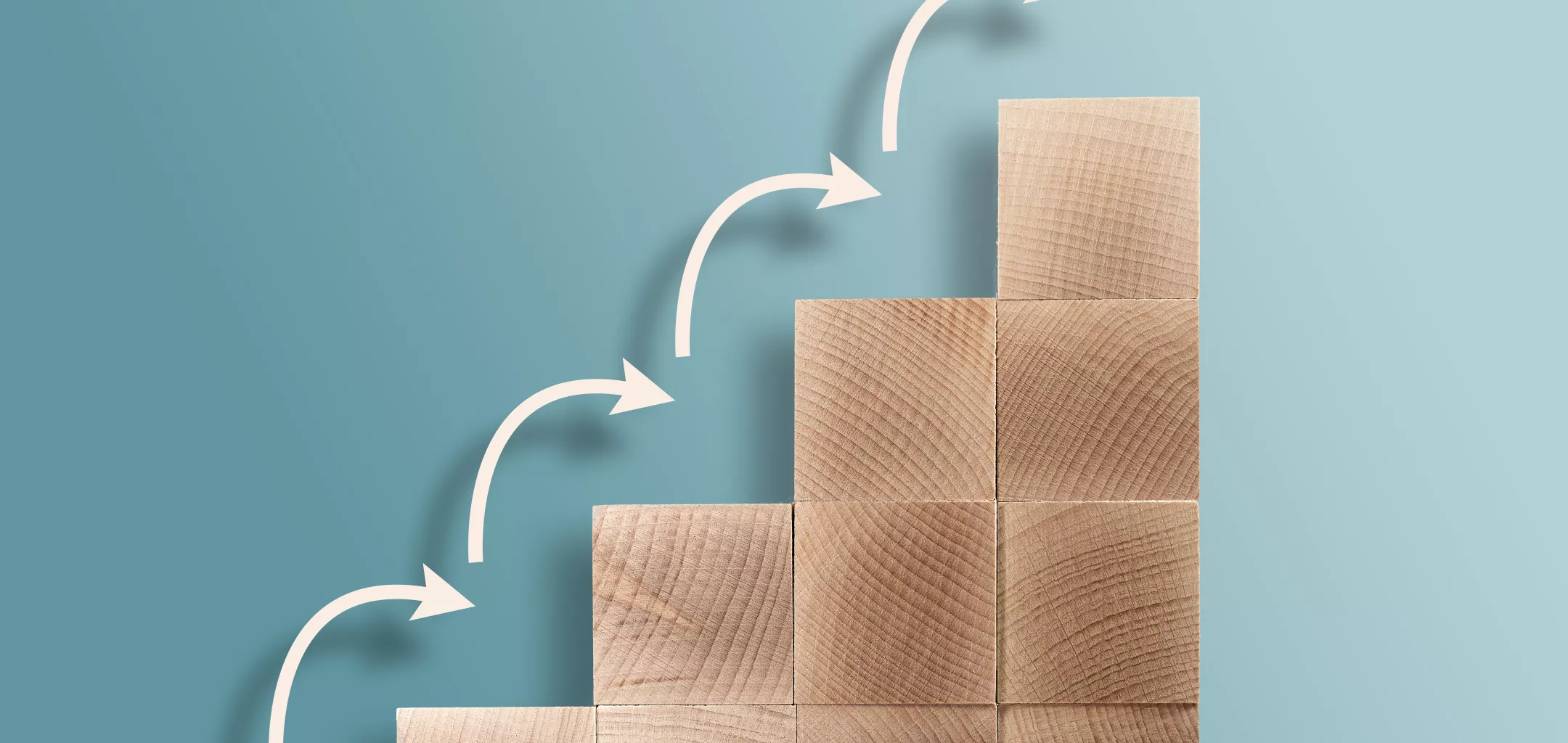 Stacked wooden blocks forming ascending steps against a blue background, with white curved arrows pointing upward from one step to the next, symbolizing growth or progress.