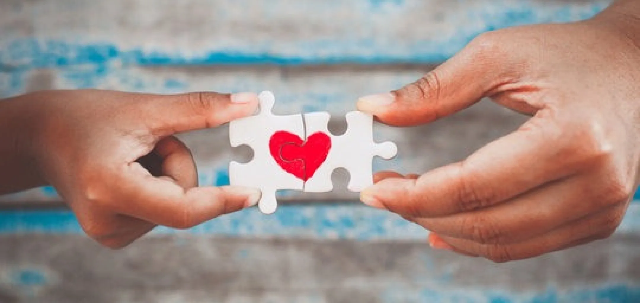 Hands connecting jigsaw puzzle piece with drawn red heart.